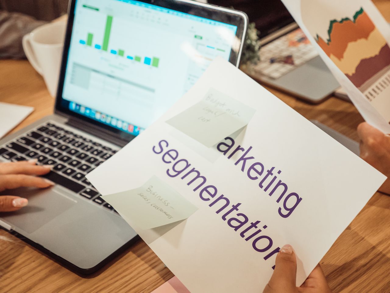 Un espace de travail moderne montrant des mains qui analysent des données marketing sur un ordinateur portable et des documents papier.